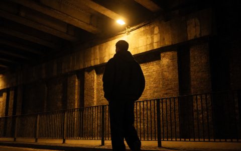 城市天桥下夜行的行人剪影,路灯把影子拉长,暗网视频相关题材的城市夜间影像
