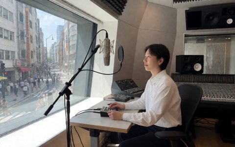 录音棚内一支指向性麦克风对着窗外街景,采集城市环境声的纪录片场景